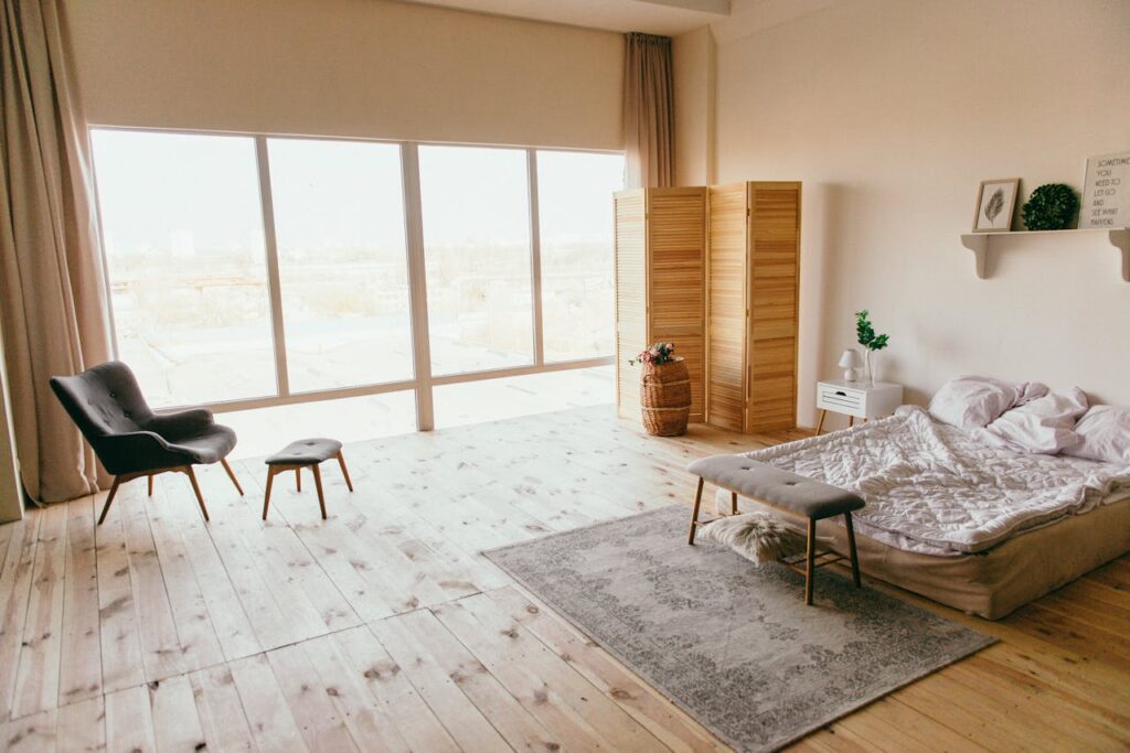 Elegant minimalist bedroom with wooden floors, large windows, and chic furniture, exuding a warm, inviting ambiance.